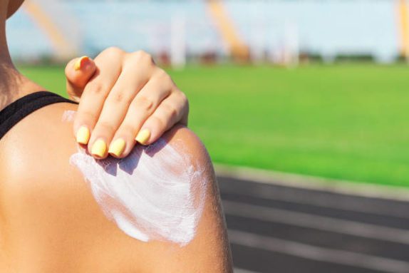 a young woman applying sunscreen to her back shoulder