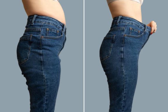 Female body before and after weight loss, diet concept. Woman is measuring waist. Belly and legs in jeans close-up.
