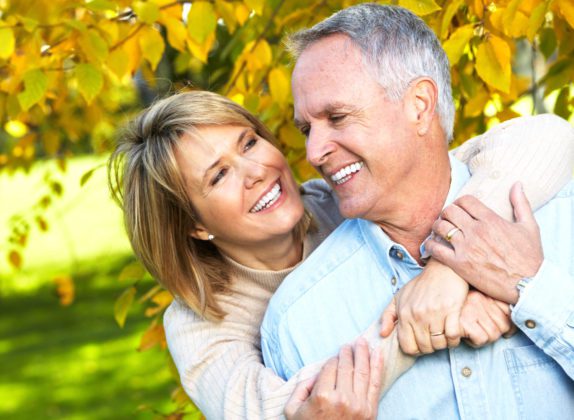 a smiling couple outside in fall, perfect candidates for a pick-me-up procedure at DeLuca Plastic Surgery